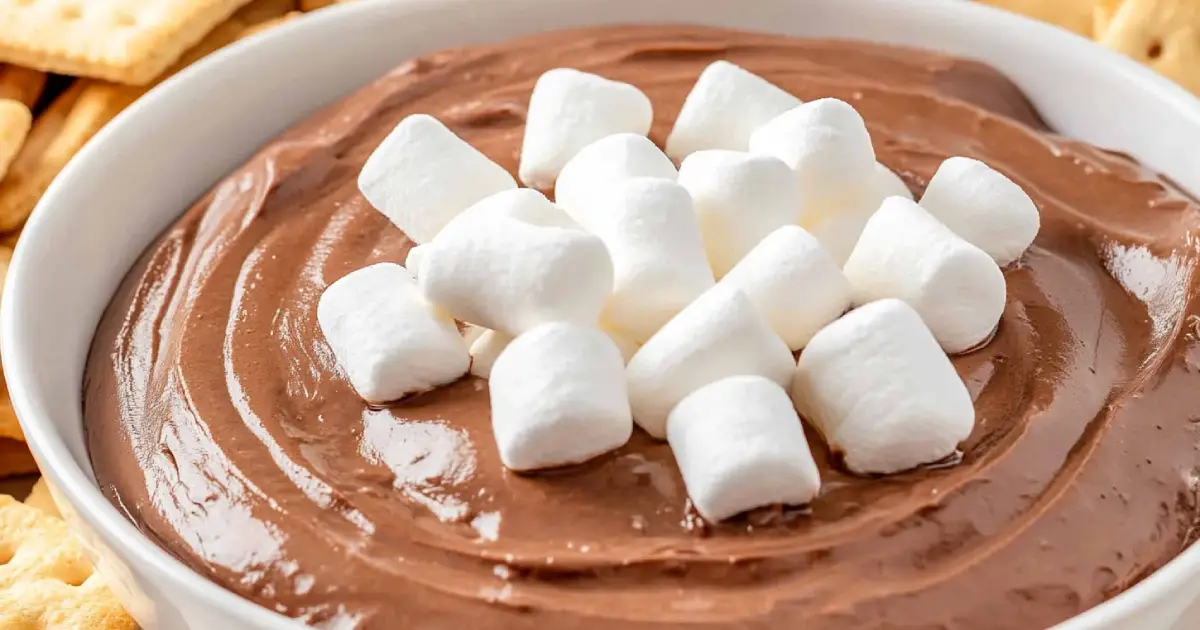 A close-up of a creamy hot chocolate dip, topped with a swirl of melted chocolate and mini marshmallows, served in a rustic bowl, with dippable treats on the side.